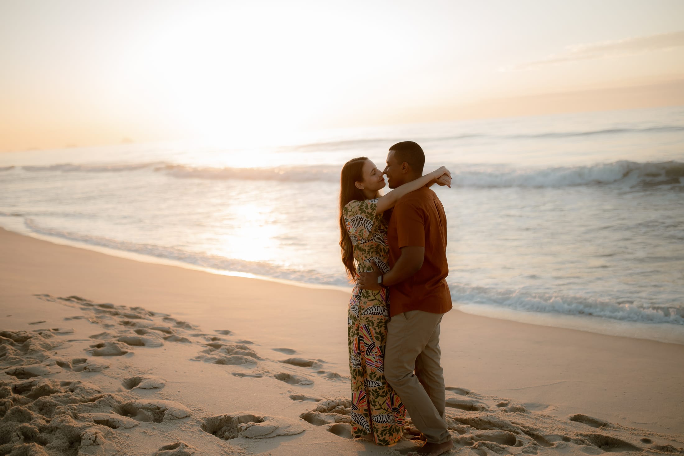 Aline e Leonardo abraçados na beira do mar, com o sol nascendo atrás